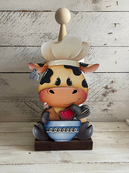 Mucca seduta con utensili da cucina Out of the Wood